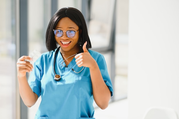 Smiling african american nurse with stethoscope holding pill