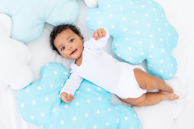 침실에 흰색 침대에 웃는 아프리카 계 미국인 작은 아이가 그의 잠옷에 놓여 있습니다