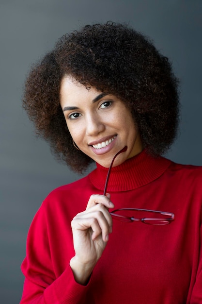 Smiling African American woman holding red eyeglasses looking at camera isolated on background