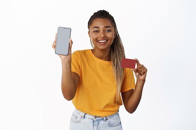 Smiling african american woman showing mobile phone screen and credit card payment app money transer and online banking concept white background