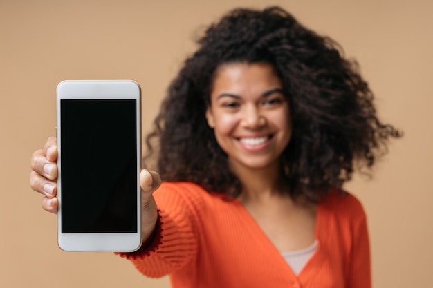 Smiling African American woman showing mobile phone screen isolated on background selective focus