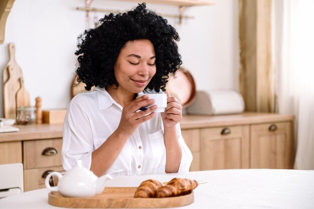 キッチンに座ってコーヒーを飲んでいる笑顔のアフリカ系アメリカ人女性