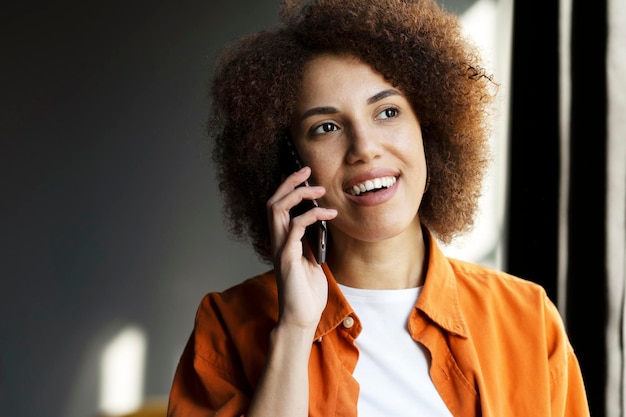 Smiling African American woman talking on mobile phone answering call looking away at home