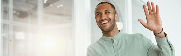 Smiling african businessman standing in modern office holding phone and waving hi to colleague