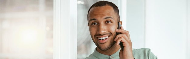 Photo smiling african businessman talking phone with client while standing in office