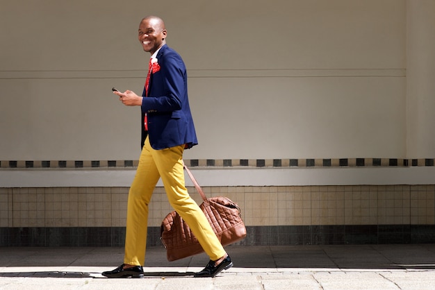 Smiling african businessman walking with bag and phone