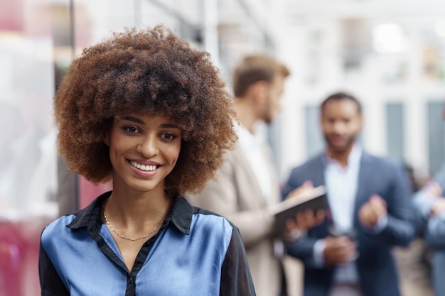 Foto sorridente donna d'affari africana in piedi in un ufficio moderno sullo sfondo dei colleghi