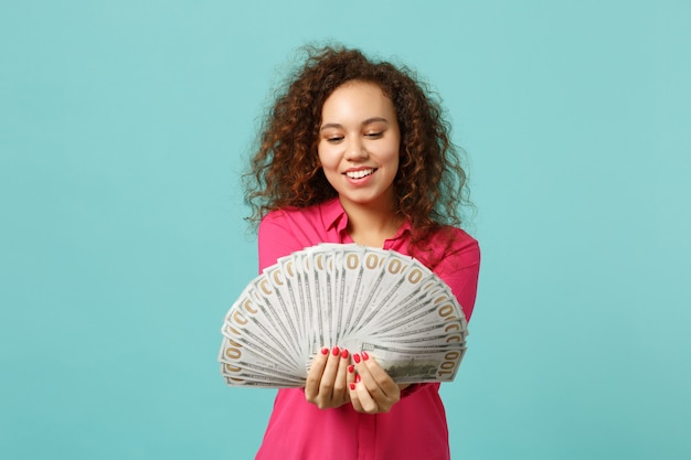 Photo smiling african girl in casual clothes holding fan of money in dollar banknotes, cash money isolated on blue turquoise wall background. people sincere emotions, lifestyle concept. mock up copy space.