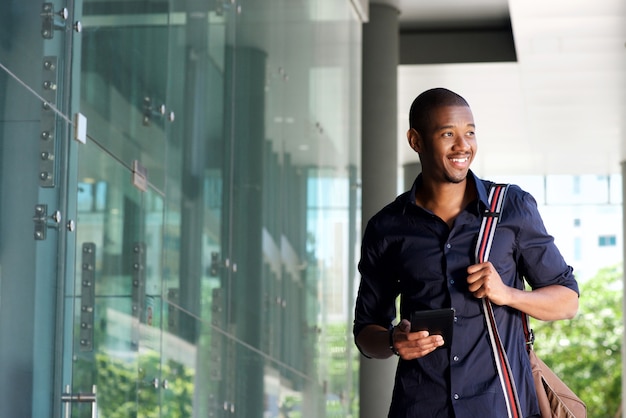 Smiling african man walking with mobile phone and bag