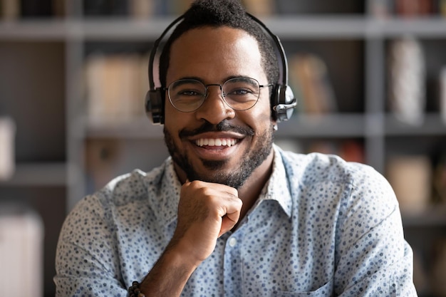 Smiling african professional telemarketer call center operator wear wireless headset look at camera afro american business man customer technical customer support service closeup headshot portrait