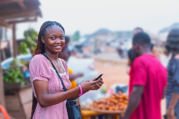 Photo smiling african saleswoman using mobile phone at fruit stand