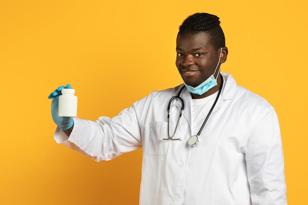 Smiling african therapist guy shows jar of pills yellow background