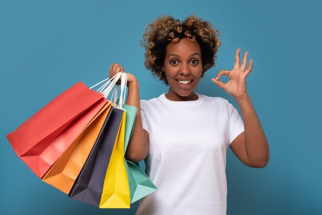 Smiling african woman with shopping bags showing ok gesture