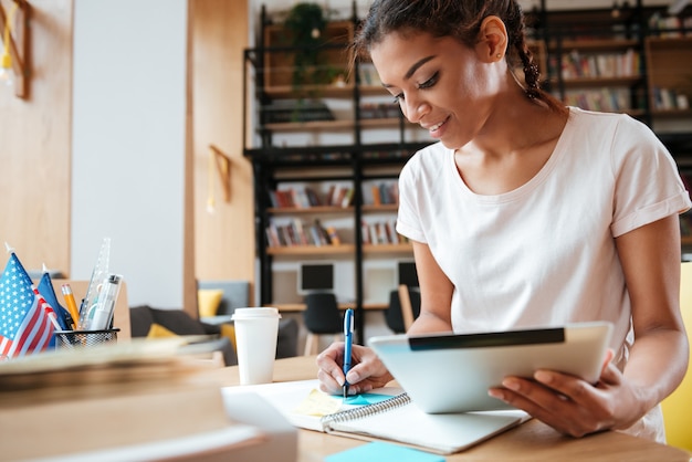 Photo smiling african woman with tablet computer in library