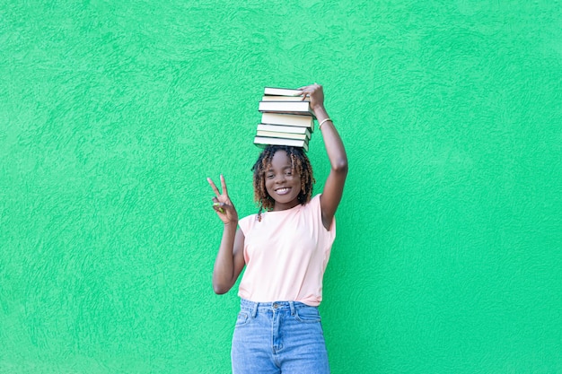 A smiling AfricanAmerican woman holds a stack of books on a green background Copy space Education