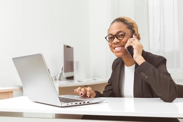 Smiling afro american business woman manager talking on the phone while sitting at the workplace.