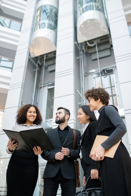 Smiling Afro-American manager holding open folder while presenting project plan to colleagues in office