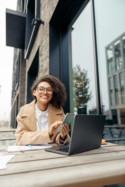 Smiling afro american woman freelancer working remotely while sitting on cafe terrace