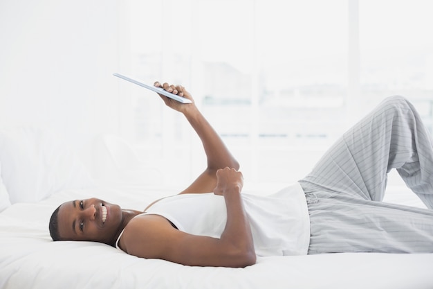 Smiling Afro man resting with digital tablet in bed