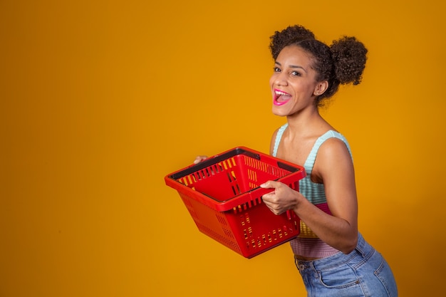 Smiling afro woman holding empty shopping basket looking at camera smiling