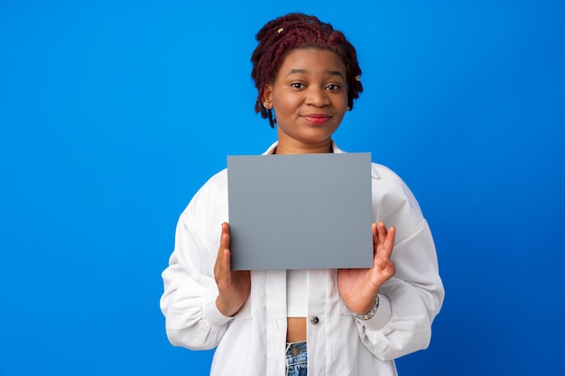 Sorridente donna afro che mostra carta grigia bianca su sfondo blu