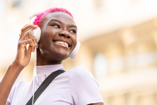 Donna afro sorridente che usa le cuffie per strada