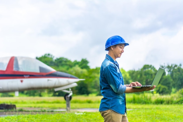 Smiling airplane mechanic using laptop while standing against airplane on land