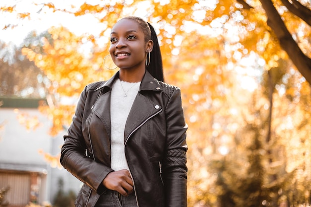 Smiling amazed african american woman dressed black leather jacket standing in the city park