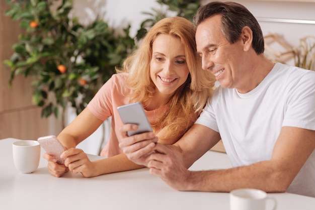 Sorridente coppia ottimista divertita che si gode il fine settimana a casa e si diverte mentre si utilizzano dispositivi digitali e si condivide la gioia