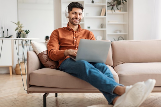 Smiling arab man using pc at home listening to music