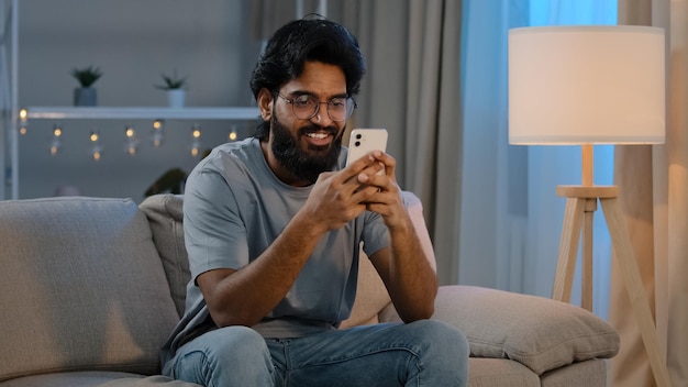 Smiling arabian indian man bearded male looking in smartphone\
smile texting with friend girlfriend