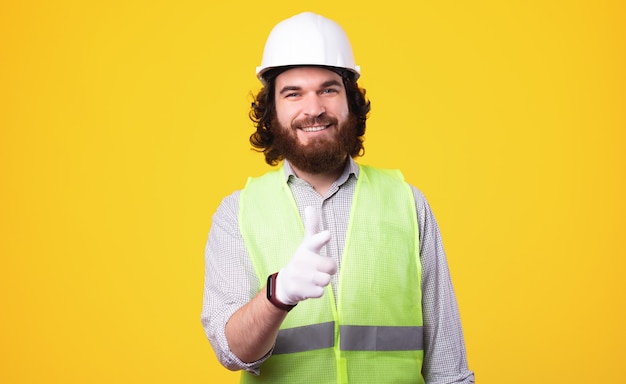 Smiling architect man standing over yellow background and pointing at the camera