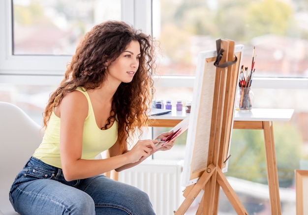 Smiling artist painting on easel