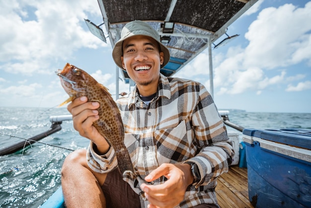 写真 小さな漁船でハタを保持している笑顔のアジアの釣り人