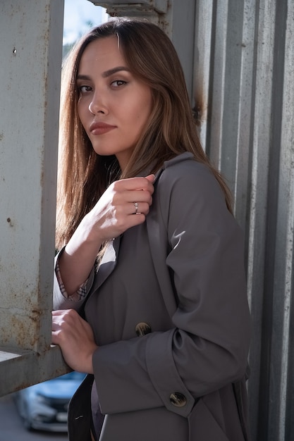 Smiling asian attractive model wearing gray trench coat standing in front of metal construction