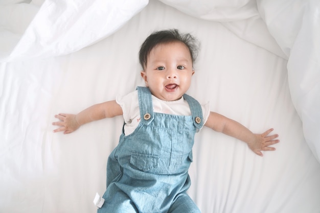 Smiling asian baby girl lying on a bed.