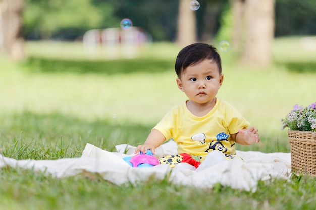 Photo smiling asian boy black hair and eyes toddler sit on white cotton in the green grass alone and playing toy.