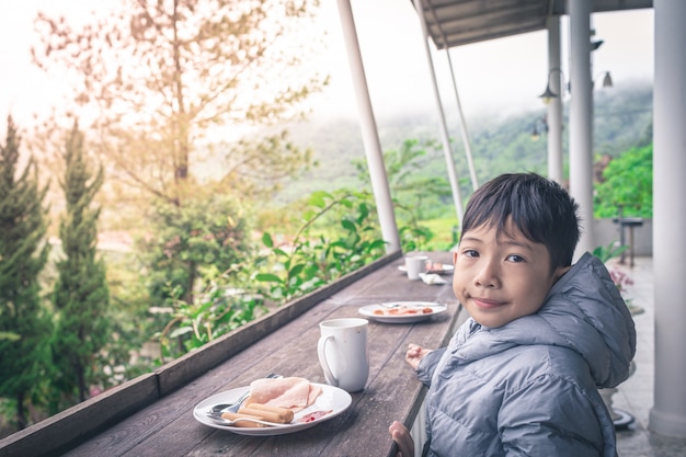 写真 笑顔のアジアの少年は美しい自然の屋外で朝食を食べています