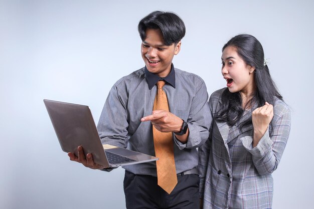 Улыбающийся азиатский бизнесмен указывает на ноутбук на руке со своим партнером с зажатым кулаком, показывая жертву
