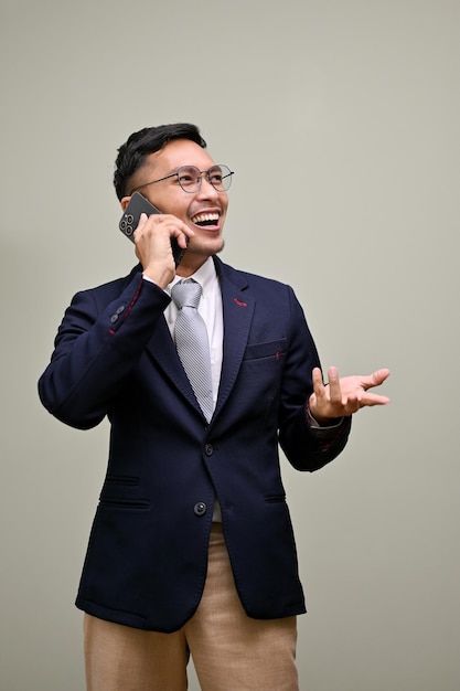 Smiling Asian businessman talking on the phone with someone standing against a green background