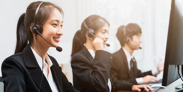 Sorridente consulente donna d'affari asiatica che indossa un microfono auricolare dell'operatore telefonico dell'assistenza clienti sul posto di lavoro.