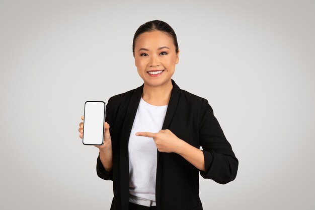 Smiling asian businesswoman presenting a smartphone with a blank screen