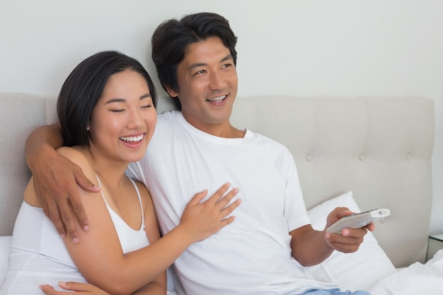 Smiling asian couple lying on bed watching tv