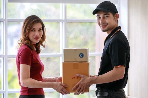 笑顔のアジアの宅配便の男性は、自宅でアジアの女性の顧客にパッケージを配信します。小包の配達と配送、ドアツードアのeコマースビジネスコンセプト。