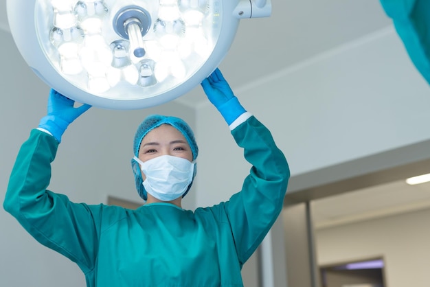 笑顔のアジアの女性外科医が手術室で手術用の照明を調整し、コピースペースを持っています。病院、医療、ヘルスケア サービス。