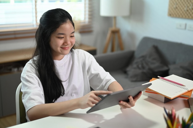 Smiling asian girl surfing internet on digital tablet in living room