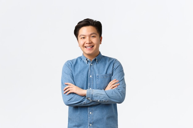 Smiling asian guy looking happy at camera, cross arms chest confident. Korean student enrolling university. Pleased man customer making choice in store, standing white background.