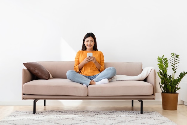 Photo smiling asian lady holding smartphone cozy home interior