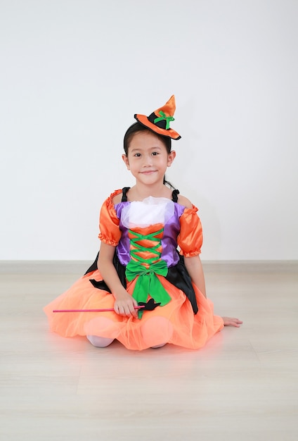 Smiling asian little child girl sitting on laminate flooring against white wall background.