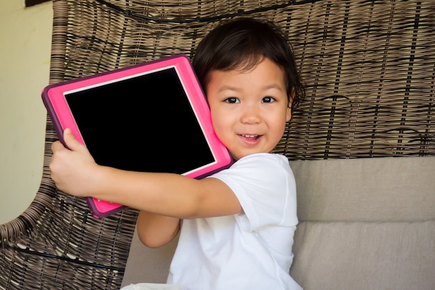 写真 彼女の手でタブレットを保持しているアジアの少女の笑みを浮かべてください。技術と子供との幸せの時間の概念。